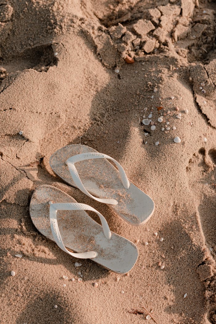 Pair of white flip flops on sand symbolizes relaxation and summertime beach vibes.