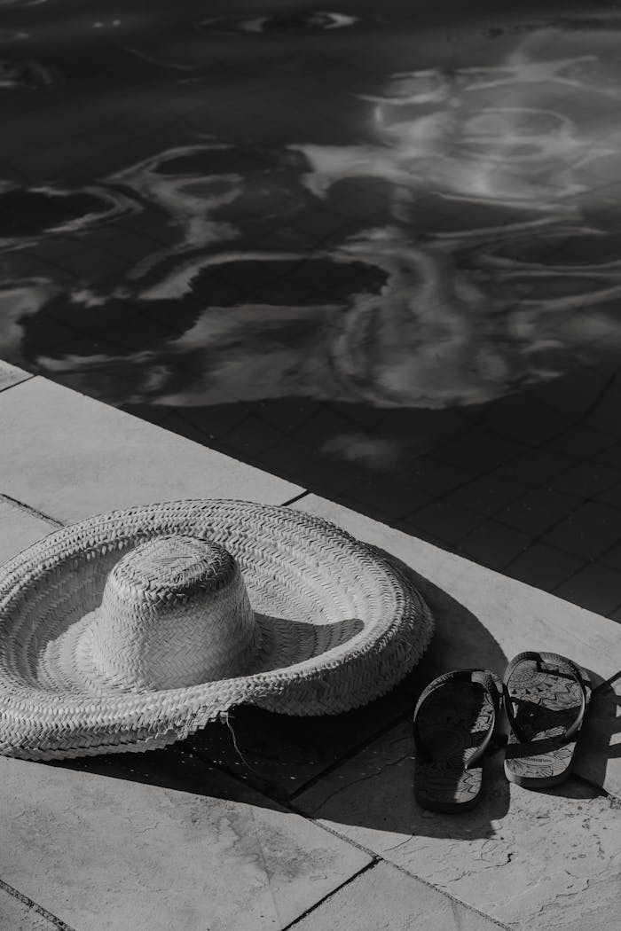Monochrome photo of a sun hat and flip flops by the poolside, reflecting relaxation.